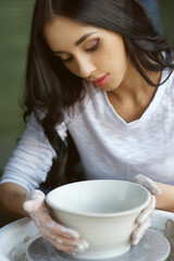 Young beautiful pretty woman with brunette dark hair working on pottery wheel and sculpting clay pot