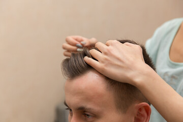 close up of hands of young barber making haircut to attractive man in barbershop