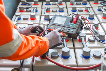 Electrician specialist inspect, check voltage and internal resistance of batteries by using battery to preventive maintenance, offshore oil and gas occupational.