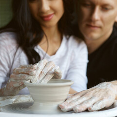 Romantic couple working on potter wheel and making or sculpting clay pot. Focus on hands.