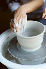 Woman working on potters wheel making dishes with their own hands. Close-up photo of dirty hands...