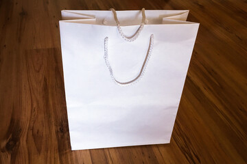 White gift bag isolated on a wooden table background. White gift box on wooden background. Gift box...