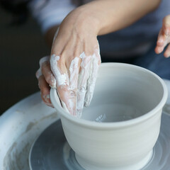 Woman working on potters wheel making dishes with their own hands. Close-up photo of dirty hands molding clay.