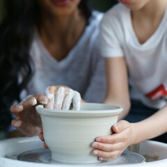 Mother teaches son to work on pottery wheel. Close up of dirty hands sculpting clay.