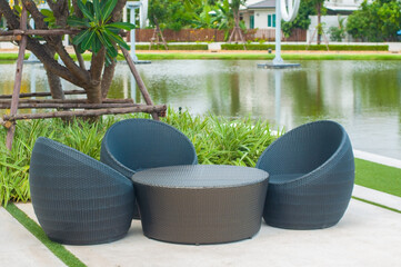 Black outdoor garden corner rattan sofa set for rest and relax next to lake in public park.