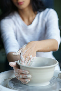 Young beautiful pretty woman with brunette dark hair working on pottery wheel and sculpting clay pot. Shallow DOF. Focus on hands
