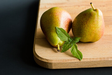 Two pears with fresh basil leaves on a wooden cutting board with black background