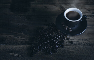 Hot coffee in black cup with coffee beans arranged on wood.