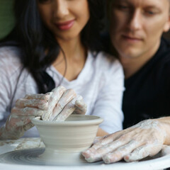 Romatic couple working on potter wheel and making or sculpting clay pot. Focus on hands.