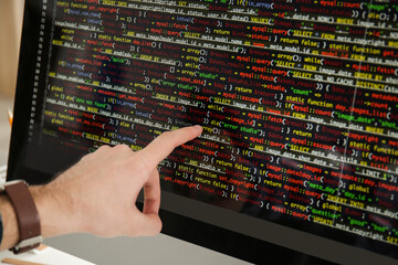 Male hand pointing on computer monitor with programming code, closeup