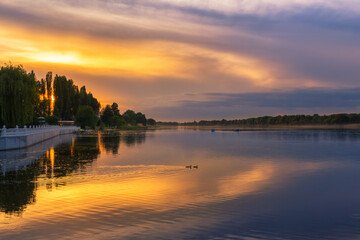 Obraz na płótnie Canvas Scenery of orange sunset at the river, dramatic evening sky reflected in the water, Khmelnytskyi, Ukraine