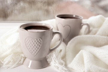 Obraz na płótnie Canvas Cups of hot drink with shawl on windowsill