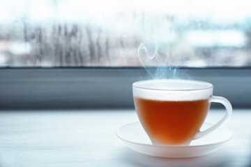 Glass cup of hot tasty drink on wooden windowsill