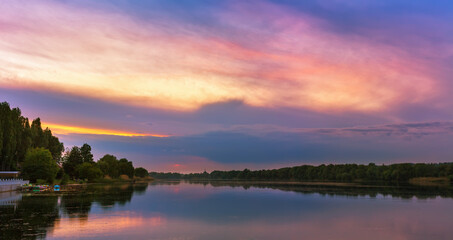 Vivid scenery of sunset at the river, colorful, dramatic evening sky reflected in the water. Khmelnytskyi, Ukraine