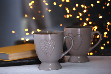 Cups of hot tasty drink with books on windowsill