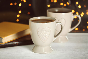 Cups of hot tasty drink with books on windowsill