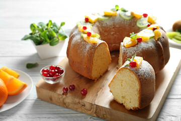 Sliced delicious yogurt cake with fruits and berries on wooden cutting board