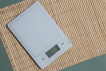 Empty kitchen scale on bamboo mat and green paper background.