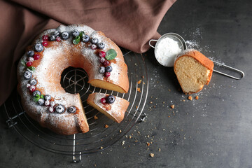 Grid with sliced yogurt cake and sugar powder in sieve on grey table