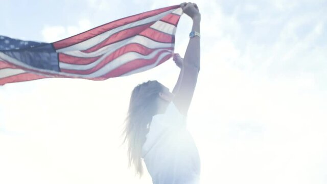 Hand held soft focused shot beautiful young blond woman standing in wind with united states flag, posing for camera, free and happy, with no care in the world, proud of her nationality