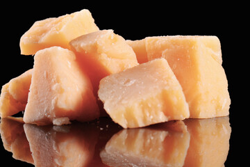 Parmesan cheese on a black glossy table with reflection. Parmesan cheese isolated on black background.
