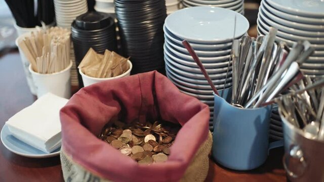 Unrecognizable teenager female customer leaves some tips in tip bag inside cafe shop after purchasing her take away coffee