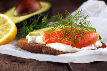 Bread with avocado and smoked salmon for lunch table. Sharing antipasti on party or summer picnic time over wooden rustic background.