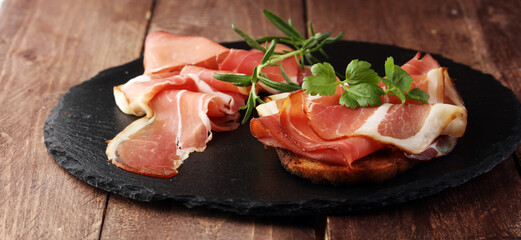 Bread with slices jamon serrano for lunch table. Sharing antipasti on party or summer picnic time over wooden rustic background.