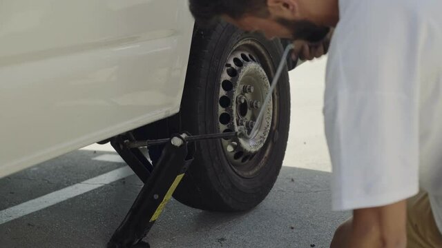 Unrecognizable Man Uses Tire Jack To Lift Up His Van To Change Flat Tire. Occasional Accident On Summer Adventure Trip Concept