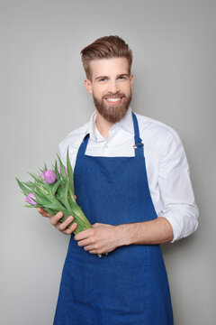 Young florist with beautiful tulips on grey background