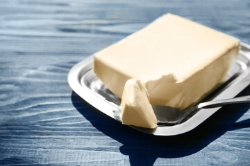 Dish with butter and shovel on wooden table, closeup