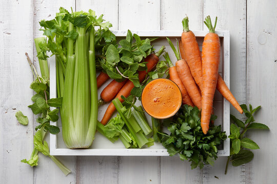 Carrot and celery juice with fresh vegetables and herbs in white wooden tray, top view