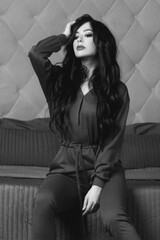 Young beautiful brunette woman sitting in bedroom. Pretty girl posing on bed in crimson red pajamas overalls