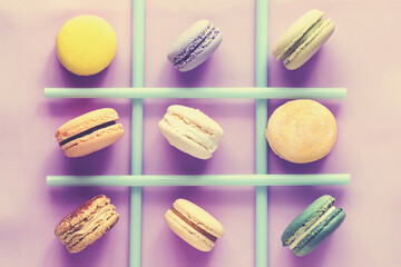 Various colorful french macaroons and straws on color background. Top view. Tic tac toe