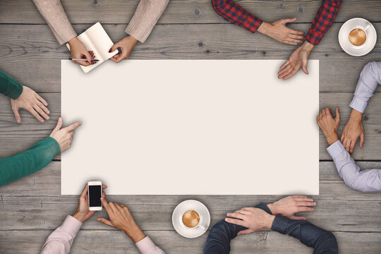 Teamwork And Cooperation Concept - Top View Of Six People Drawing Or Writing On A Large White Blank Sheet Of Paper.