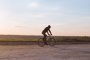 Fototapeta na wymiar Alone rider on fixed gear road bike riding in the desert near river, hipster tourist bicycle rider pictures.