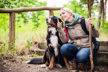 Hiking woman with rucksack and her bernese mountain dog on a trail