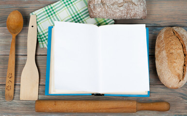 Open recipe book on wooden background, spoon, rolling pin , green checkered tablecloth.