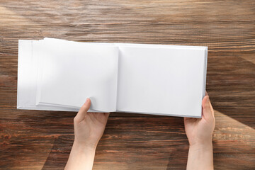 Obraz premium Female hands holding opened book with blank pages on wooden background