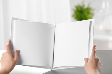 Female hands holding opened book with blank pages on light background