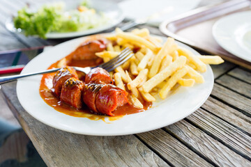 Snacks to beer on a white plate. Bavarian fried sausages, fried potatoes, chips on a wooden table background.