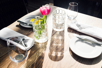 restaurant on the canal Venice. Tulip in a vase. table setting for a lovey dinner. Empty glasses set in cafe. Part of interior. napkins, plates, and cutlery.