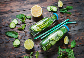 Cold and refreshing infused detox water with lime, mint and cucumber in a bottle on wood background