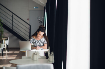 Smiling female writing something in her notebook while sitting at a desk with a laptop.