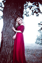Obraz na płótnie Canvas Fashion gorgeous young blonde woman in beautiful red dress in a fairy-tale forest. magic atmosphere. toning shot