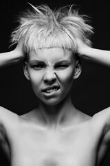 Close up on face of crazy mad cocky young woman with stylish dyed pink hair, hands ruffle her haircut angry and bold expression on black studio background