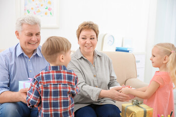 Obraz premium Happy senior couple and their grandchildren exchanging gifts at home