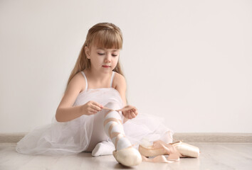 Beautiful little ballet dancer tying pointe shoes in light dance studio