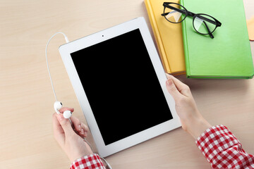 Woman holding earphones and tablet on table. Concept of audiobook
