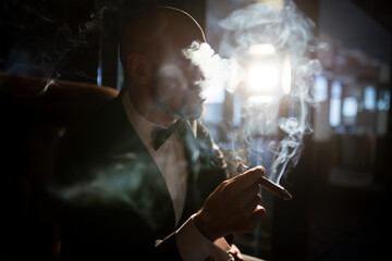 A brutal man in a dress coat smokes a cigar.